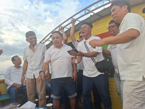 Foto 6. Nyanyian di atas kapal dalam perjalanan menuju Pantai Meat, Jumat 24 Juli 2026.Sebuah speaker portabel di tengah geladak sudah cukup untuk mengubah perjalanan menjadipertunjukan bersama.