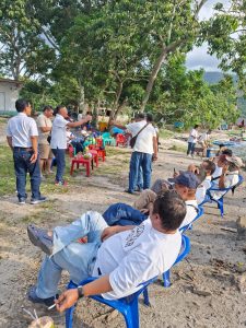 Foto 10. Rombongan Grup Koor Kaum Bapak HKBP Ressort Slipi bersantai di tepi PantaiMeat, Balige, Jumat 24 Juli 2026. Kursi-kursi dijajarkan menghadap Danau Toba di bawahrindang pepohonan, dengan warung kelapa muda di sisi kanan.