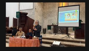 Foto 1 — Pdt. Daniel Taruli Asi Harahap, M.Th. menyampaikan khotbah "Merawat Perkawinan" dengan tayangan slide "3 — Sekolah Seumur Hidup" di layar proyektor, didampingi dua orang panitia di meja depan. HKBP Ressort Slipi, Kamis 2 Juli 2026.
