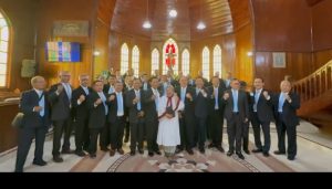 Foto 19. Rombongan Grup Koor Kaum Bapak (Ama) HKBP Ressort Slipi berfoto bersama dihalaman depan Gereja HKBP Balige, seusai Ibadah Minggu, 26 Juli 2026. Bangunan gerejakayu bergaya gotik dengan menara menjulang dan jendela kaca patri ini merupakan salah satupenanda sejarah kekristenan di Tanah Batak. Tampak pula pelayan gereja setempat berdiri bersama rombongan.