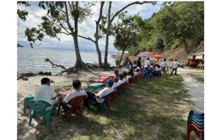 Foto 8. Rombongan Punguan Koor Ama HKBP Slipi bersantai di tepi Pantai Meat, Balige, Jumat 24 Juli 2026. Kursi-kursi dijajarkan menghadap Danau Toba di bawah rindang pepohonan, dengan warung kelapa muda di sisi kanan.